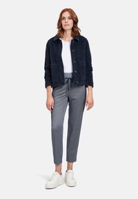 Granatowa kurtka teksturowana z dwoma przednimi kieszeniami, zapięcie na guziki, biała koszulka, szare spodnie w wzory i białe sneakersy.