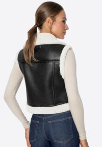 Chaleco corto de cuero sintético negro con un cuello y forro de forro polar blanco. Presenta una textura suave y una forma ajustada.