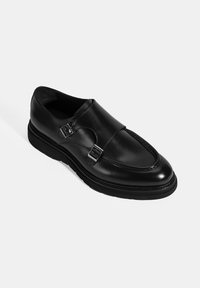 Black leather dress shoe with double buckle accents, rounded toe, stitched detailing, and a textured black rubber sole.