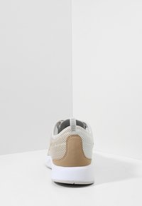 Sporte skor med en ovandel i nät i ljus beige och vit, med en slät tan mockaaccent på hälen och en vit texturerad sula.