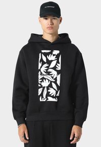Sudadera negra con un gráfico blanco de diseños florales enmarcados en forma rectangular. Fabricada con una suave tela de sudadera y con capucha ajustable.