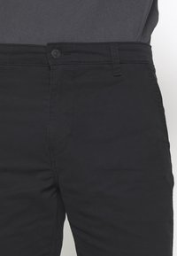 Černé kalhoty vyrobené z měkkého materiálu, s knoflíkovým zapínáním, poutky na opasek a hladkým, ne texturovaným povrchem.