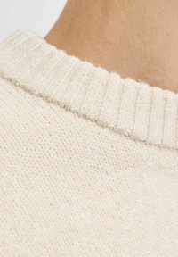 Cremefarvet strikket sweater med ribbet krave, der har et struktureret mønster og blød finish, som fremhæver et tæt på billede af halsudskæringen.