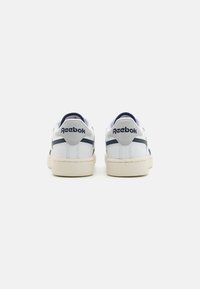 Reebok'i spordijalatsid, millel on valge nahk pealis, tumesinised detailid ja tekstuuriga beež kummist tallad, logoga kandadel ja minimaalne disain.