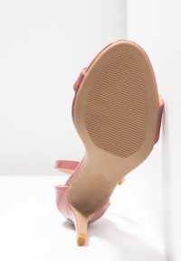 Sandale à talon haut rose avec semelle texturée et sangle, vue de dessous sur fond blanc.