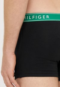 Cuecas boxer pretas com cintura elástica verde e branca com o nome da marca "HILFIGER". O material parece macio e elástico.