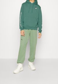 Grön hoodie med framficka och logotyp, i kombination med ljusgröna sweatpants med sidofickor. Bärs med vita träningsskor.