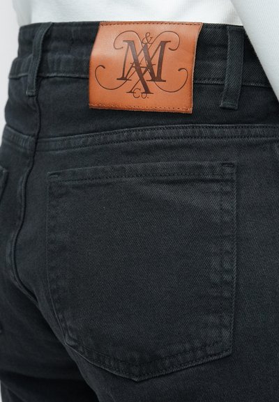 Jean en denim noir avec une pièce en cuir embossée du logo à l'arrière de la ceinture. Le jean possède des poches traditionnelles et des coutures ton sur ton.