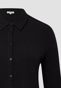 Zwart langslavenshirt met een kraag, voorzien van subtiele textuur, knopen aan de voorkant en een moderne pasvorm. Merktag zichtbaar bij de hals.