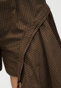 Καφέ και μαύρο ύφασμα με καρό σχέδιο, με λεπτομέρεια πτυχώματος ή πτυχωτής φάσας, που δείχνει υφή και ραφές σε κοντινό πλάνο.