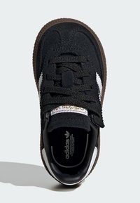 Sorte semskede sneakers med brun gummisåle, hvite side-striper, teksturerte laces og gulllogo-detalj på tungen. Ovenfra.