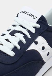Saucony sneakers with a navy upper, white accents, textured material, flat white laces, and a branding logo on the tongue.