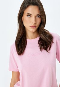 Camiseta de algodón rosa con mangas cortas y cuello redondo, que presenta la palabra bordada "Creativo" en una fuente sutil a lo largo del pecho.