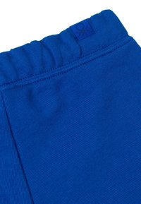 Pantaloni di cotone blu con una texture a coste e una fascia elastica in vita, caratterizzati da una piccola etichetta nera con logo sulla cintura.