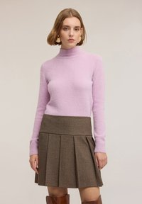 Jasnofioletowy, miękki sweter z golfem o mieszanym splocie, zestawiony z brązową plisowaną spódnicą w kratę. Gładka faktura, dopasowany krój i subtelne detale.