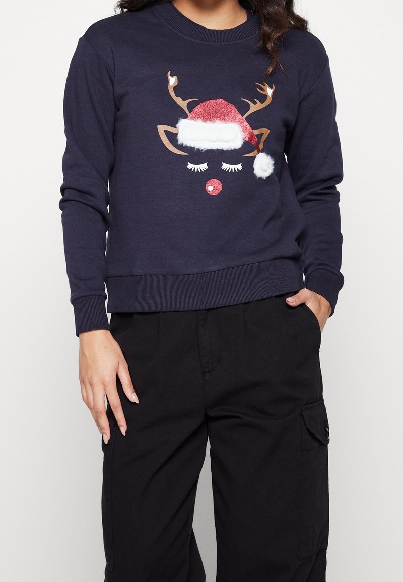 Felpa blu navy con grafica di una renna, con cappello rosso glitterato, pon pon bianco e occhi ricamati. Polsini e orlo a coste.