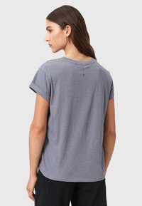 Camisa de algodón gris con mangas cortas enrolladas, corte relajado y detalle en la costura trasera. La tela tiene un aspecto suave y ligeramente texturizado.
