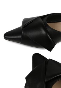 Svarta läderskor med spetsig tå och vikdesign. Har en mjuk textur och en elegant silhuett.