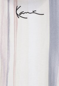 Puha szövet függőleges csíkokkal pasztell bézs, krémszínű és szürke árnyalatokban, a bal felső sarokban egy kis fekete, aláírás stílusú logóval.