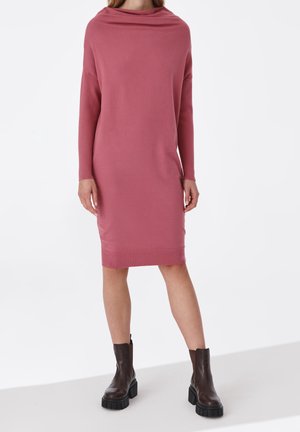 Femme portant une robe-pull rose poussiéreux à manches longues et longueur au genou, avec des bottines épaisses marron foncé.
