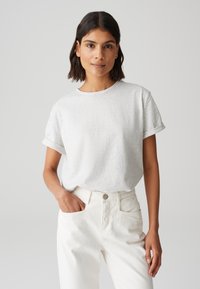 T-shirt gris clair avec des manches courtes retroussées, encolure ronde, fabriqué à partir d'un matériau doux. Associé à un pantalon blanc taille haute avec des poches avant.