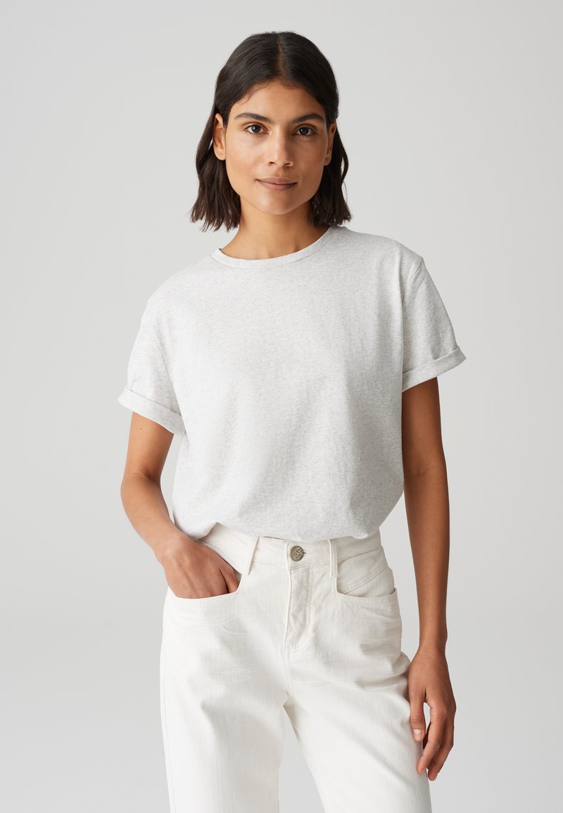 T-shirt gris clair avec des manches courtes retroussées, encolure ronde, fabriqué à partir d'un matériau doux. Associé à un pantalon blanc taille haute avec des poches avant.