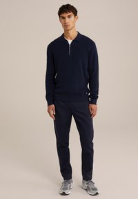 Marinblå stickad tröja med dragkedja vid kragen, matchad med marinblå byxor och grå sneakers. Snygg design, åtsittande form och texturerat tyg.