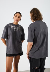 T-shirt en coton gris avec un graphique de serpent sur le devant, à manches courtes et à coupe décontractée. Le dos est uni avec une finition lisse.