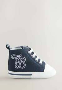 Navy modri platneni čevelj z visokim zgornjim delom z belim gumijastim prstnim pokrovom in podplatom. Ponaša se z vezenim logotipom "TB" in belimi vezalkami. Teksturirana površina, oblazinjen ovratnik.