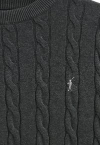 Suéter de punto cable gris oscuro con un alto cuello acanalado, que presenta un pequeño logo de contraste de un golfista. La textura es gruesa y suave.