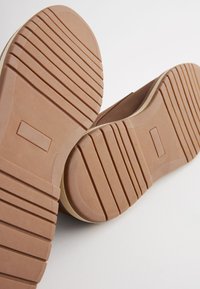 Suole di scarpe in gomma color marrone chiaro con scanalature orizzontali e verticali per una migliore aderenza. Bordi arrotondati e una superficie liscia e piatta.