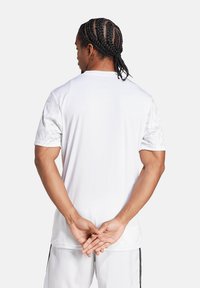 Wit sportshirt met korte mouwen, met textuuraccenten op de schouders. Materiaal lijkt glad en lichtgewicht.
