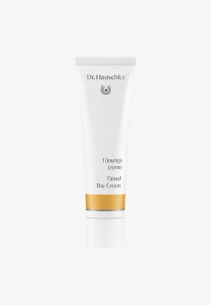 Tubetto di plastica bianco con dettagli argento e oro. Il testo dice "Crema Tönungs Dr. Hauschka Tinted Day Cream." Texture liscia, forma cilindrica.