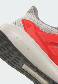 Tige en mesh gris, accents rouge vif et une semelle intermédiaire épaisse couleur crème avec le logo "CLOUDFOAM". Semelle extérieure noire texturée avec motif de bande de roulement.