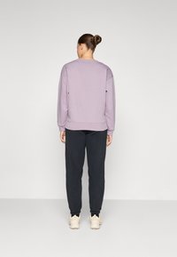 Lilac pullover with a round neck and dropped shoulders, paired with dark trousers. Smooth fabric with a relaxed fit and ribbed cuffs.