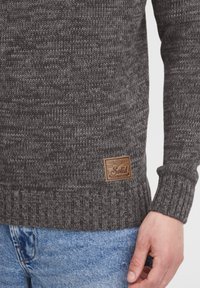 Grijs gebreid sweater met geribbelde mouwen en zoom, voorzien van een leren label met "Solid." Draag over lichtblauwe denim jeans.