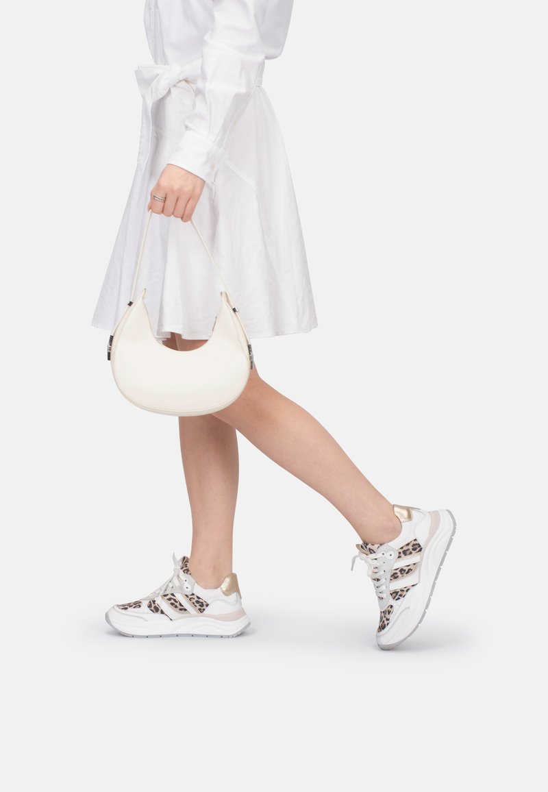 Pochette blanche au design incurvé, associée à des baskets blanches avec un imprimé léopard et des accents dorés, portée avec une robe chemise blanche.