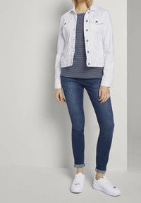 White denim jacket with two chest pockets, striped blue and white T-shirt, blue jeans, and white sneakers with laces.