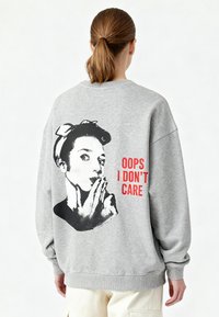 Felpa grigia in tessuto morbido con una grande grafica in bianco e nero sulla schiena e testo rosso con la scritta "OOPS I DON’T CARE."