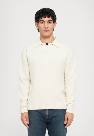Crèmekleurige sweater met een kraaghals, ribgebreide mouwen en zoom. Gemaakt van een textuurbreisel. Draagt gecombineerd met blauwe jeans.