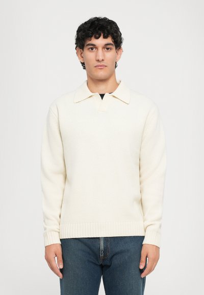 Cremefarvet sweater med krave, ribbede manchetter og kant. Lavet af et struktureret strikmateriale. Båret med blå jeans.