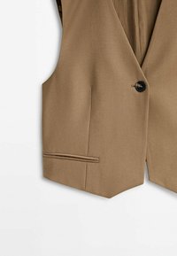 Gilet marron clair sur mesure avec un seul bouton noir et une poche passepoilée sur le côté gauche sur fond blanc.