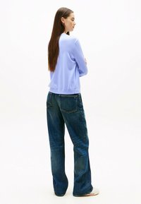 Lichtpaarse sweatshirt met een ronde halslijn, gecombineerd met losse, blauwe denim jeans met achterzakken. Over het geheel een gladde textuur.