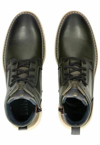 Botas de cuero verde hasta el tobillo con puntera redonda, parte delantera con cordones y suela beige en contraste. Presenta acentos en tono ladrillo y una plantilla acolchada.