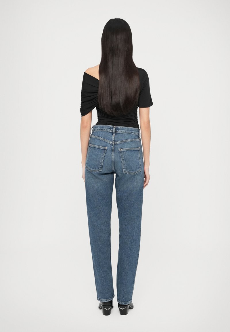 Blauwe denim spijkerbroek met hoge taille en rechte pijpen, vier zakken en zichtbare stiksels, gecombineerd met een zwart off-shoulder topje.