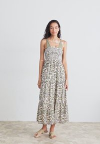 Maxi dress in lightweight fabric featuring a zebra print in green and tan, with a fitted bodice and tiered skirt. Paired with beige sandals.