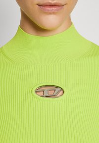 Lime green ribbed turtleneck top featuring an oval cutout with silver hardware detail at the center. Smooth texture and fitted design.
