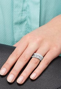 Tre anelli impilati in metallo color argento, caratterizzati da fasce lisce e testurizzate, con piccoli accenti circolari e una finitura lucida.