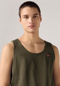 Olíva zöld ujjatlan pamut trikó kerek nyakkivágással és egy kis piros Levi's logóval hímzett elöl. Sima textúra.