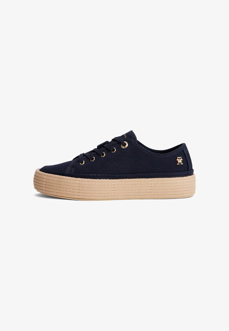 Baskets basses bleu marine avec semelle plateforme beige texturée et œillets dorés, avec un petit logo doré sur le côté près du talon.
